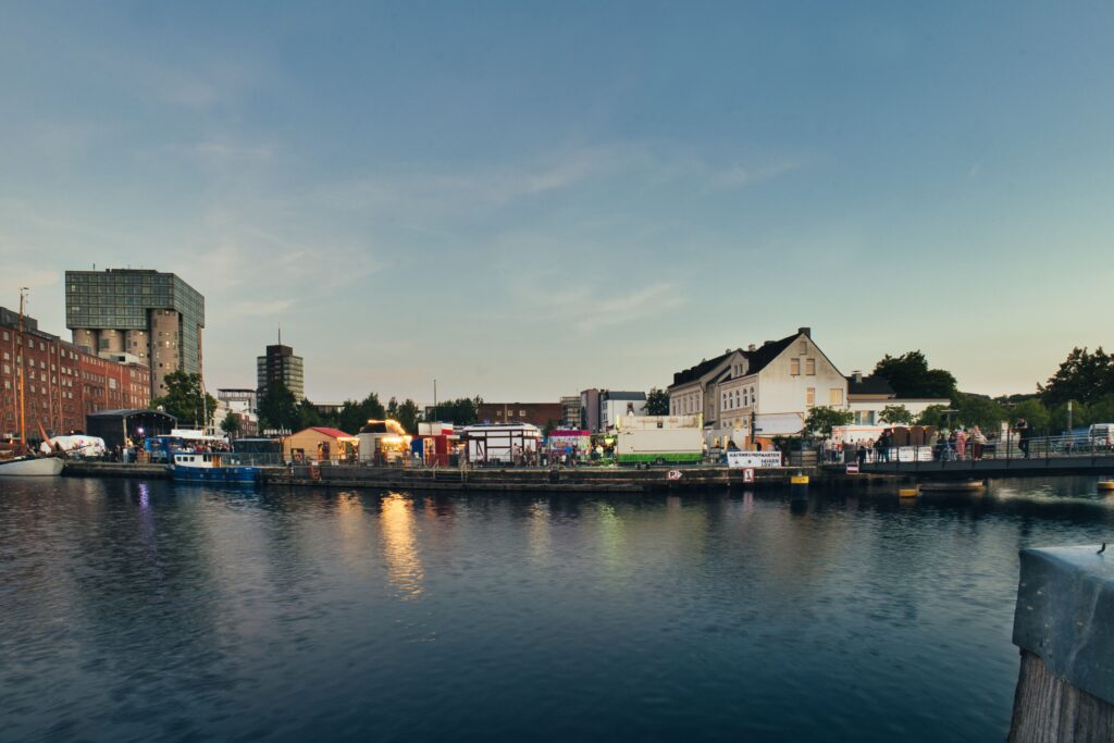 Evening view of a lively urban harbor with buildings and calm water reflections.